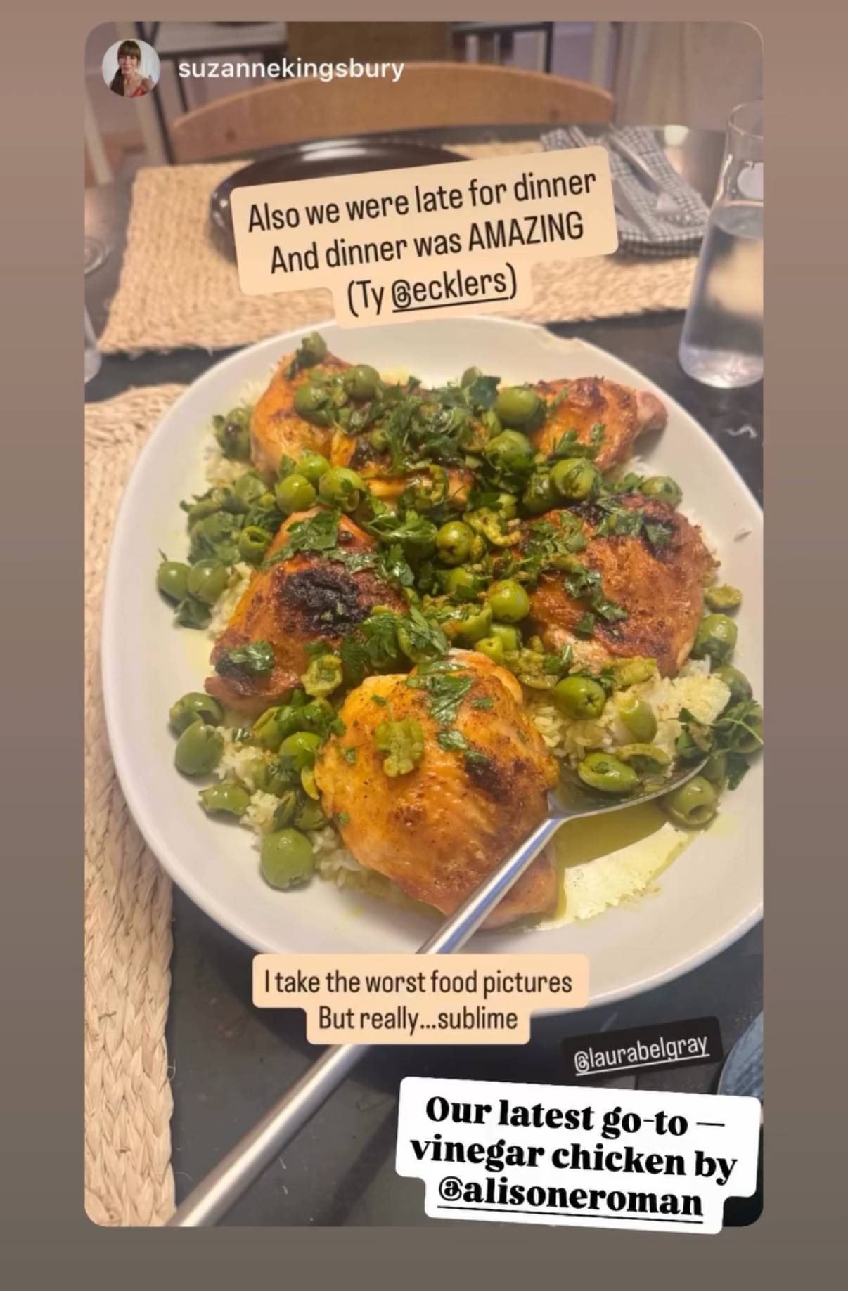A screenshot of an Instagram Story posted by @suzannekingsbury featuring a large serving platter of roasted chicken pieces over rice, topped with green olives, herbs, and sauce, with a serving spoon resting in the dish. The Story text reads: “Also we were late for dinner And dinner was AMAZING (Ty @ecklers).” Another caption says: “I take the worst food pictures But really…sublime.” At the bottom, Suzanne tags @laurabelgray and shares, “Our latest go-to — vinegar chicken by @alisoneroman.” The table is set with woven placemats, plates, and a glass of water in the background.