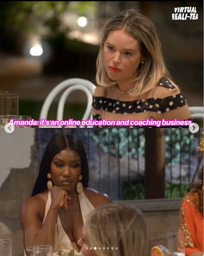 Still image from a reality TV show showing two people seated at an outdoor dining table at night. In the foreground, a person with dark skin, long straight black hair, and large gold earrings rests their chin on their hand while looking toward someone off camera. Behind them, a person with light skin and shoulder-length blonde hair looks forward with a focused expression. Glassware and plates are on the table. On-screen text reads, “Amanda: it’s an online education and coaching business,” with a “Virtual Real-Tea” watermark in the top-right corner.