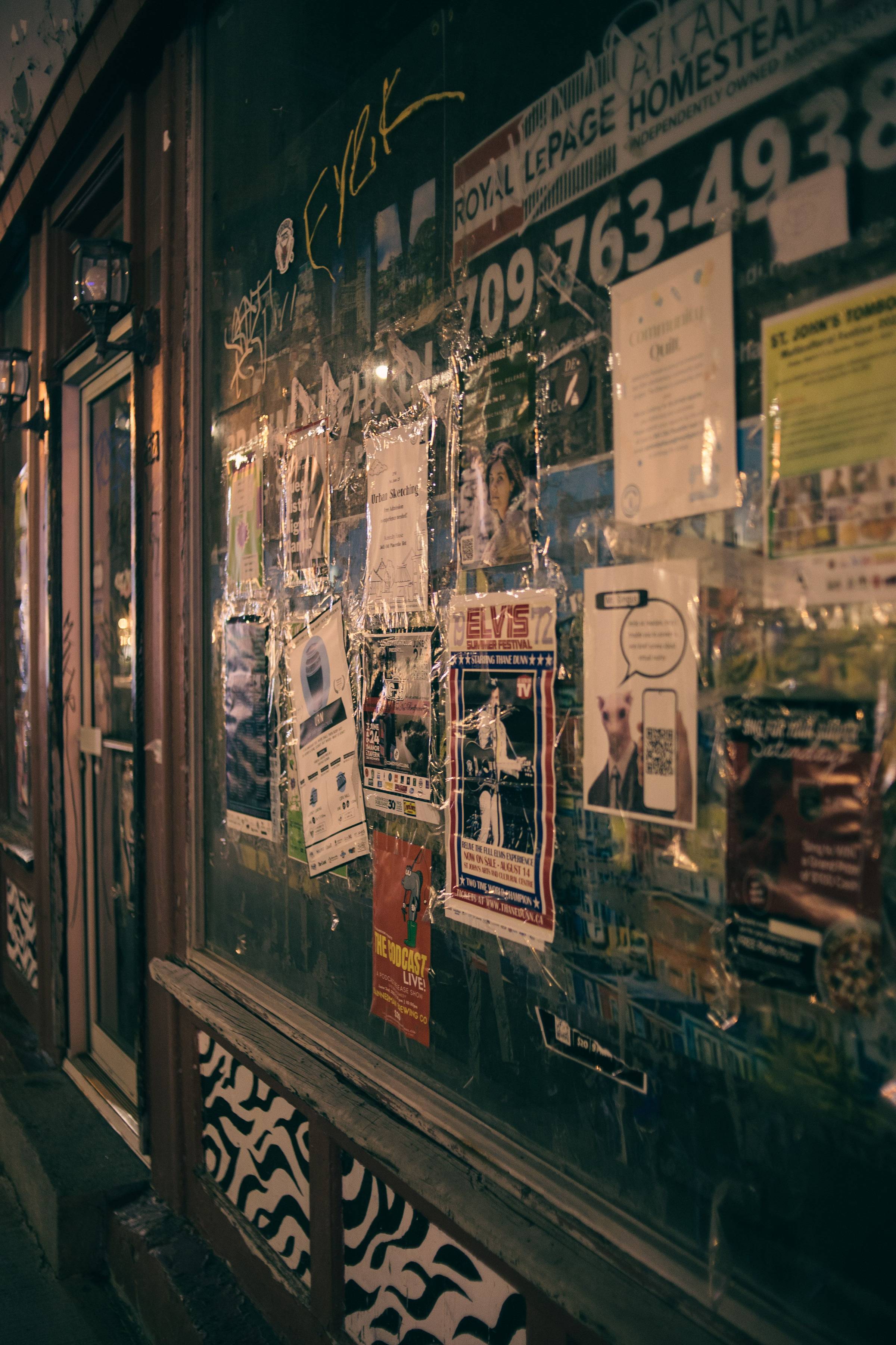 Close-up view of a glass window with diverse posters at night, depicting advertising.