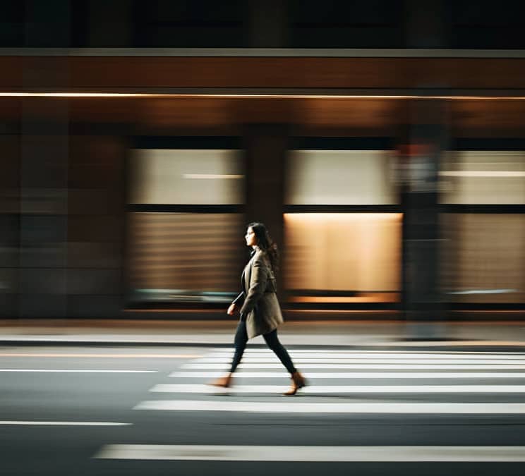 Person walking across a city crosswalk with motion blur, representing forward momentum and leaving unhelpful habits behind.