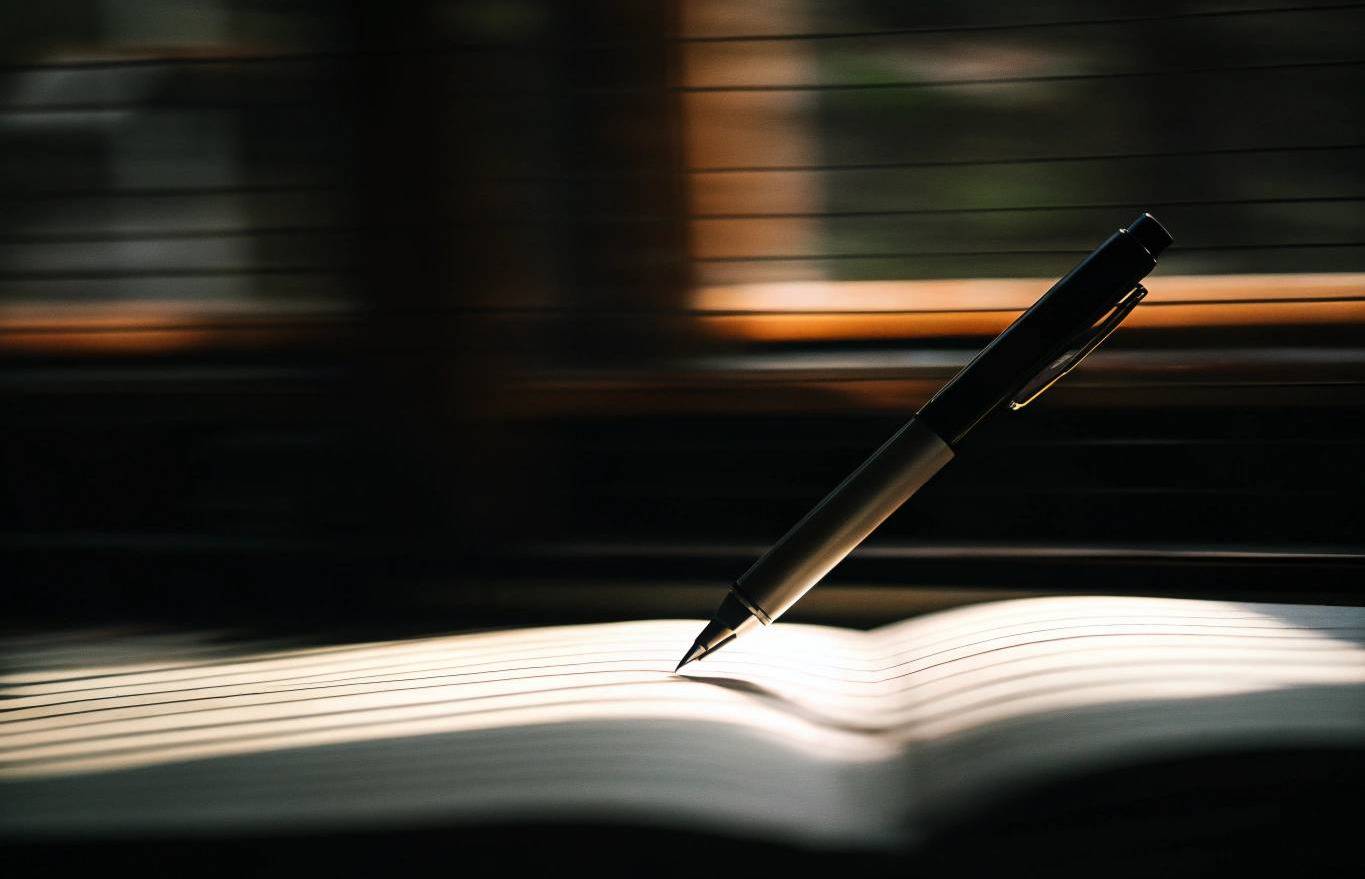 Black pen resting on an open lined notebook with subtle motion blur, symbolizing imperfect progress and taking action.