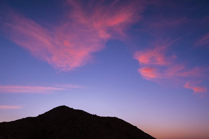 Pink clouds drift across a twilight sky over mountain.