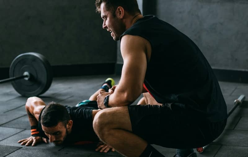 A trainer assists someone doing push-ups.