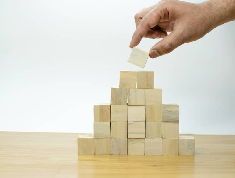 A hand is placing a piece of wood into a pyramid