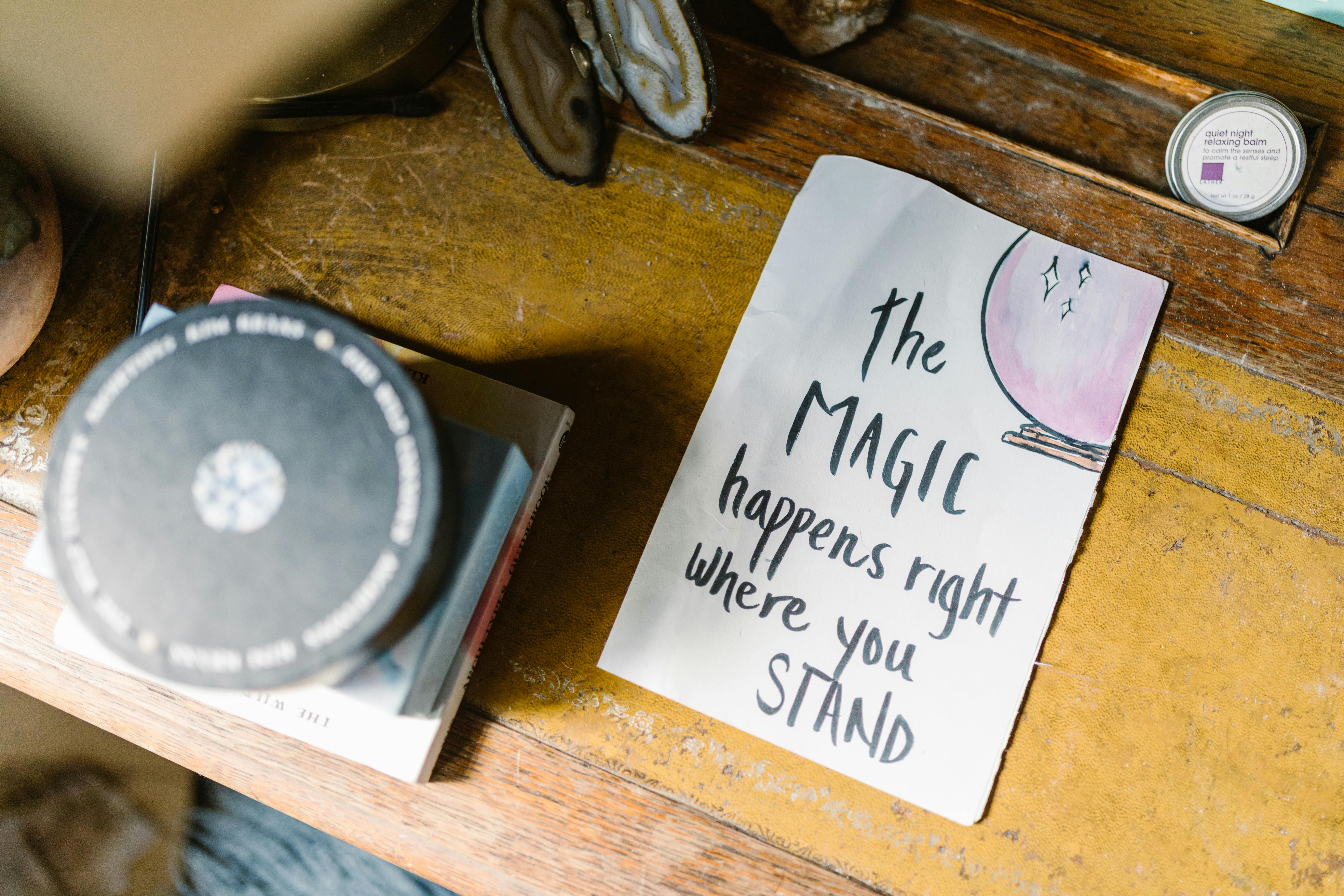 piece of paper on wooden table that reads "the magic happens right where you stand"