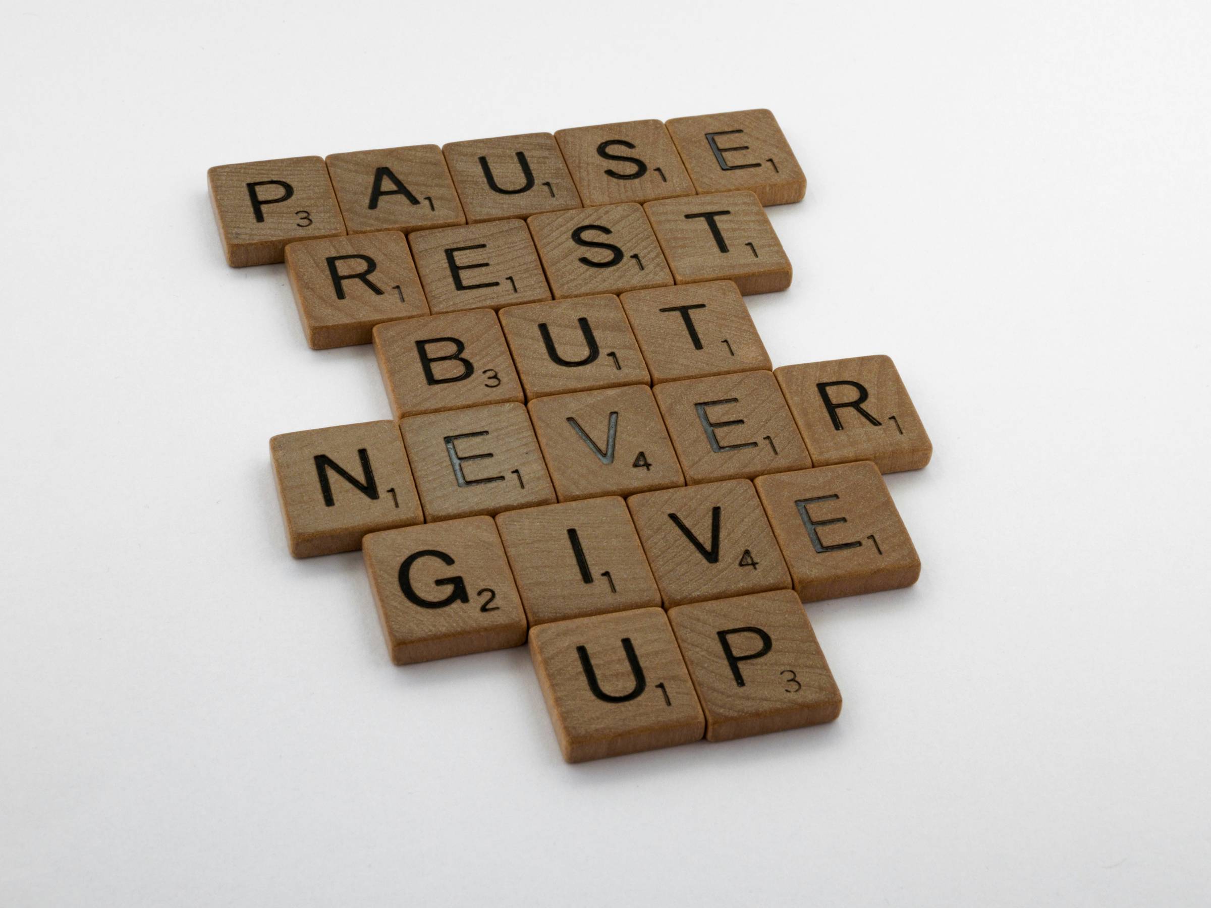 wooden tiles on white surface that read "pause, rest, but never give up"