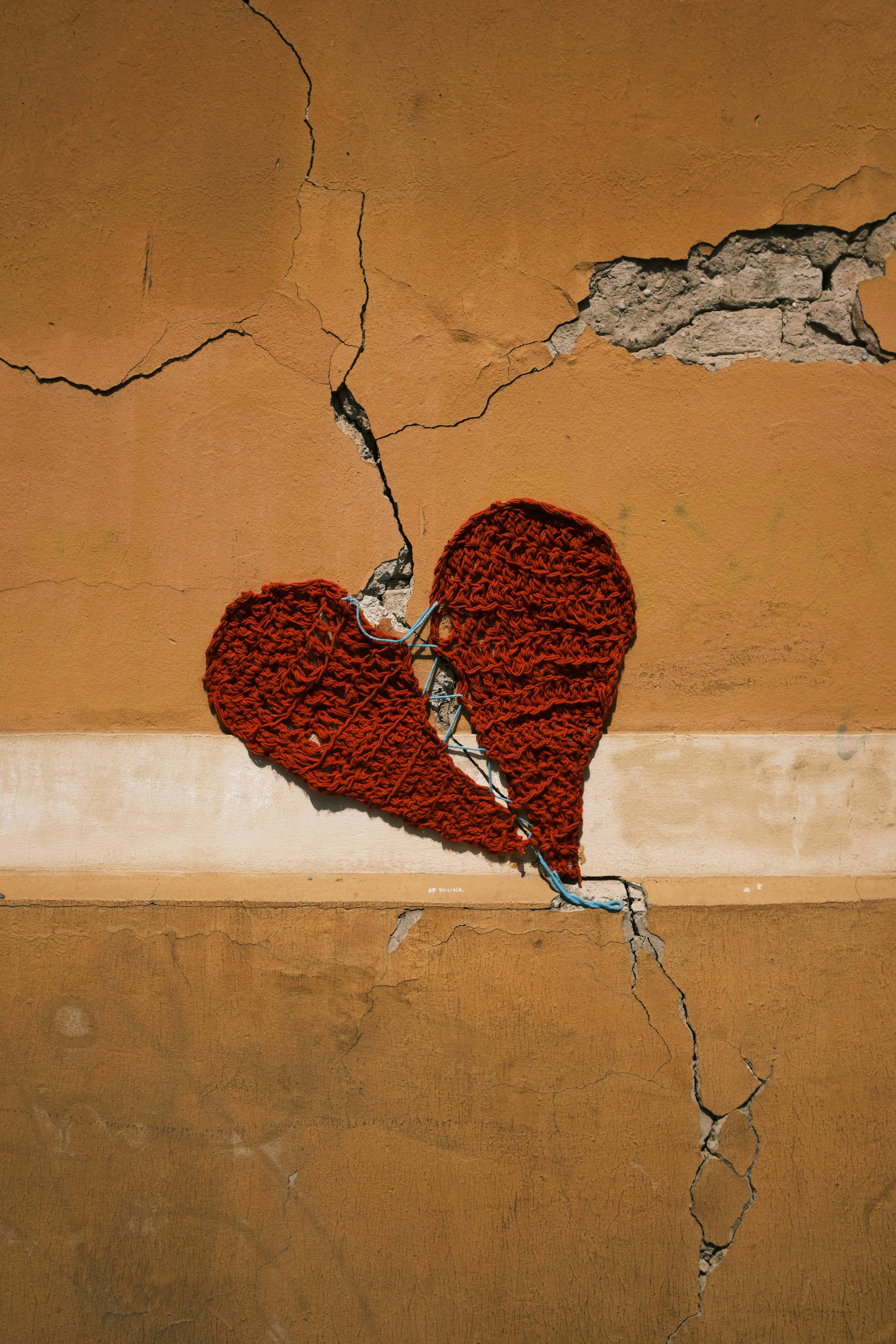 to halves of a knitted heart in red stitched together and attached to an orange wall