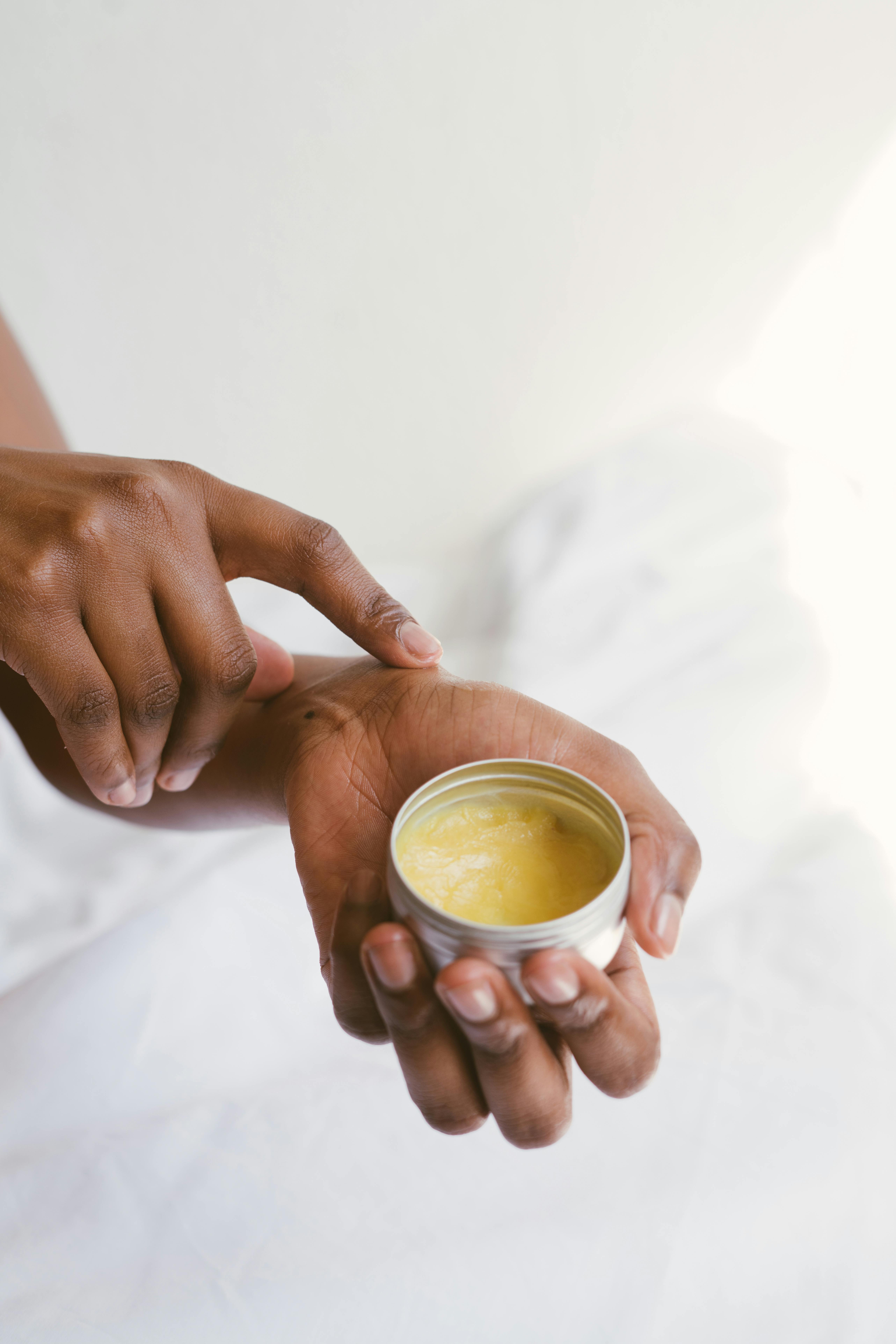 brown person holding a balm on one hand and applying it with the other hand