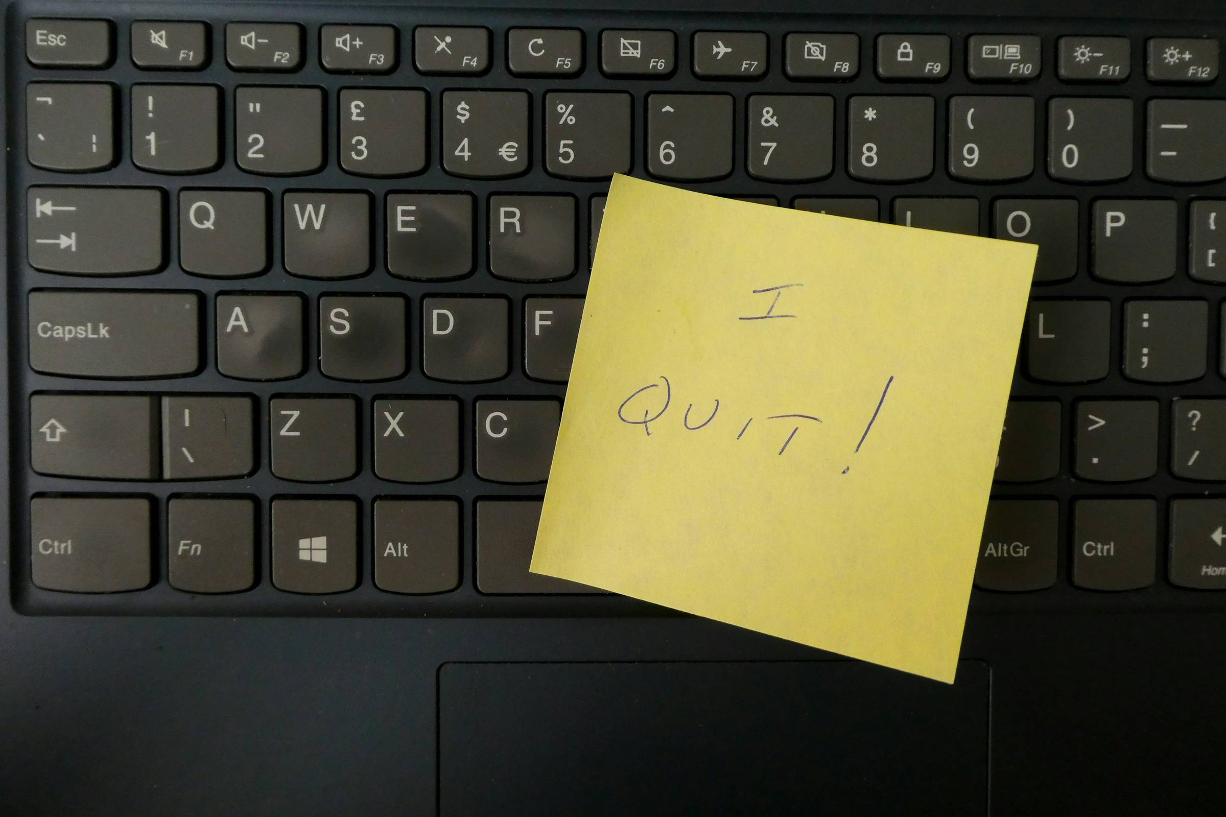 a yellow notepad on a keyboard with the handwritten message "I quit!"