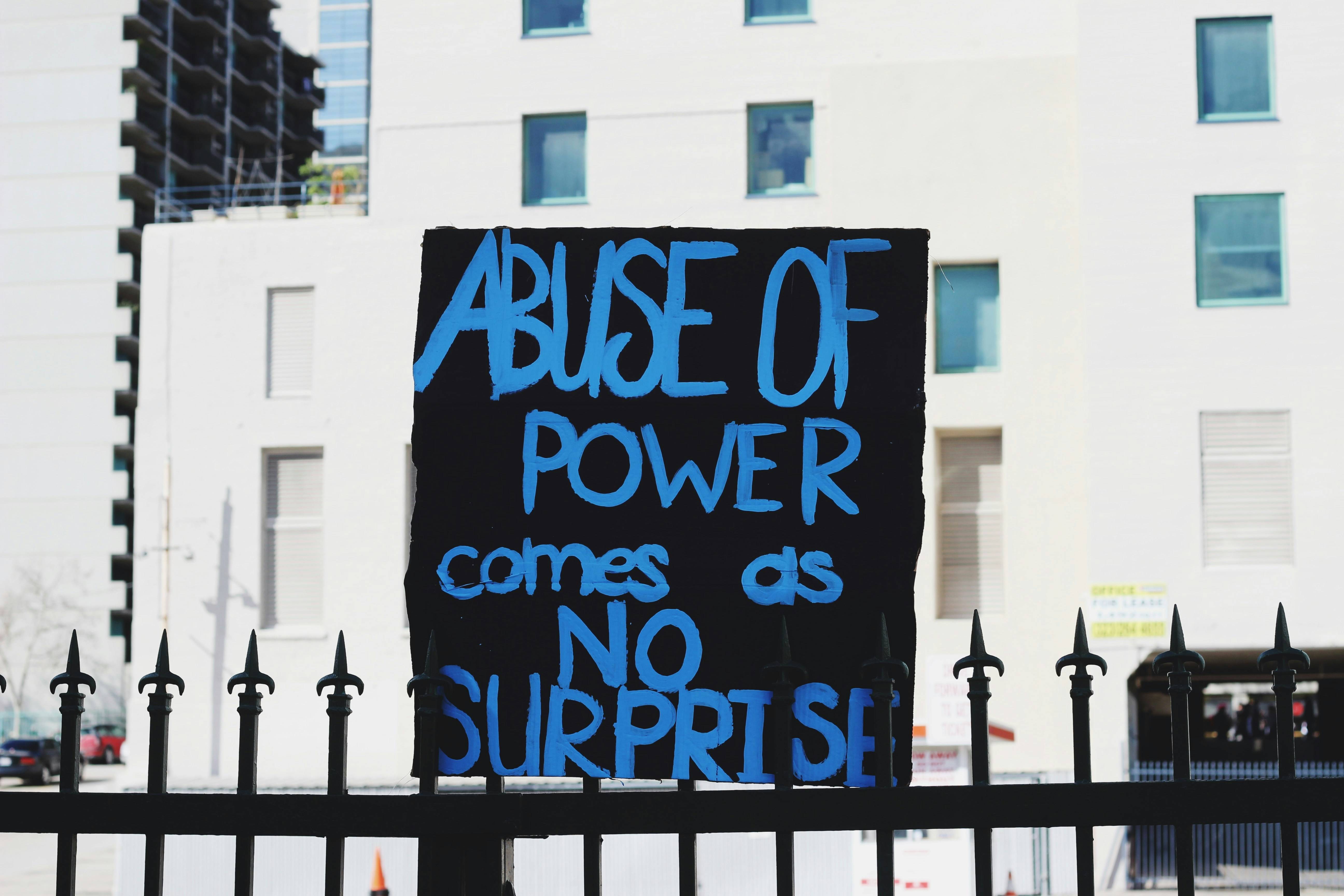 sign on a street that reads "abuse of power comes as no surprise"