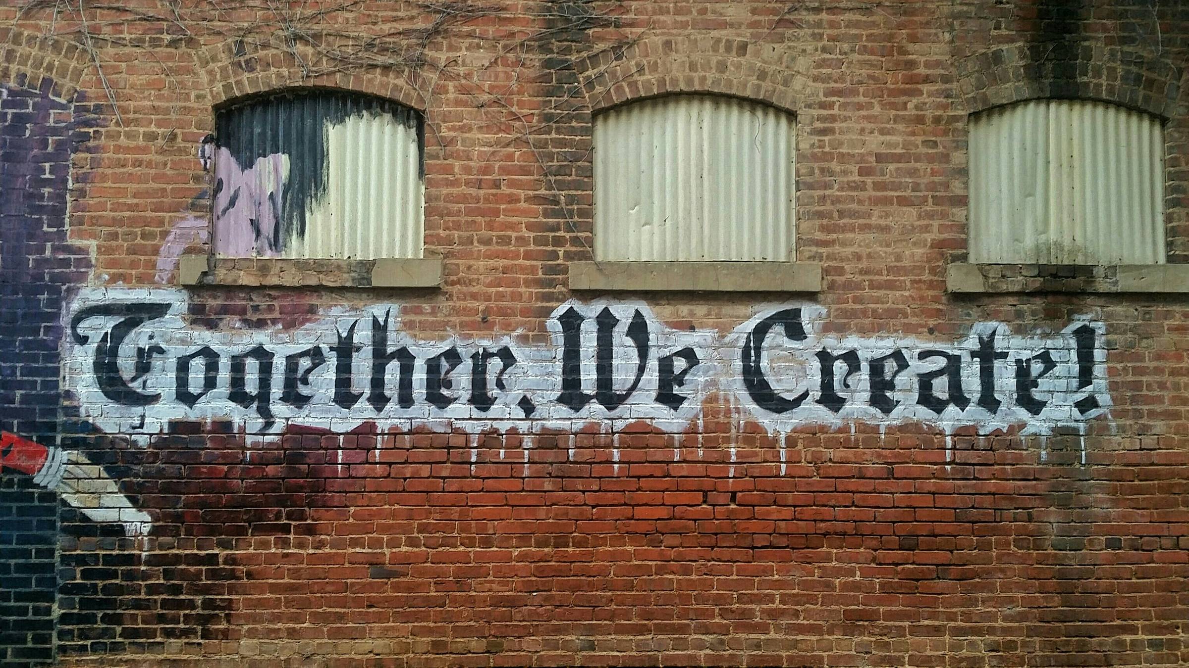 graffitti on a brick wall that reads "together we create"