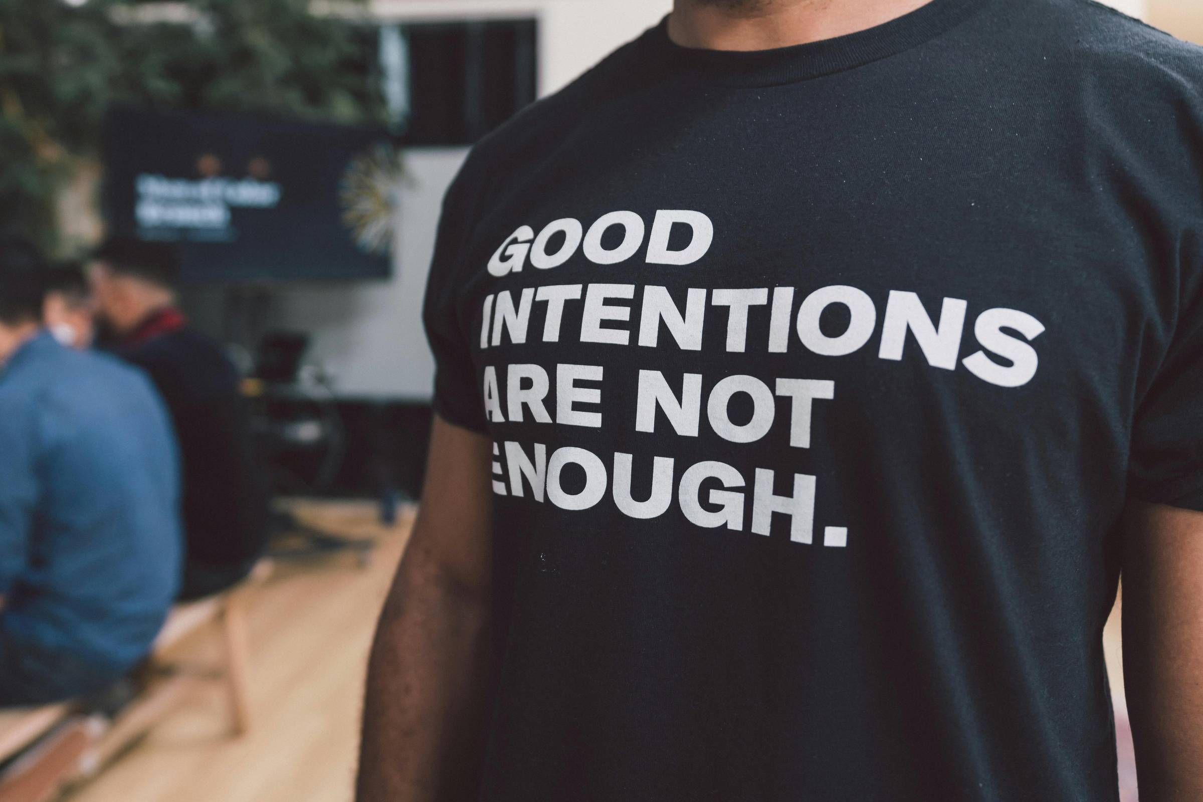 person wearing a black shirt with white letters that read "good intentions are not enough"