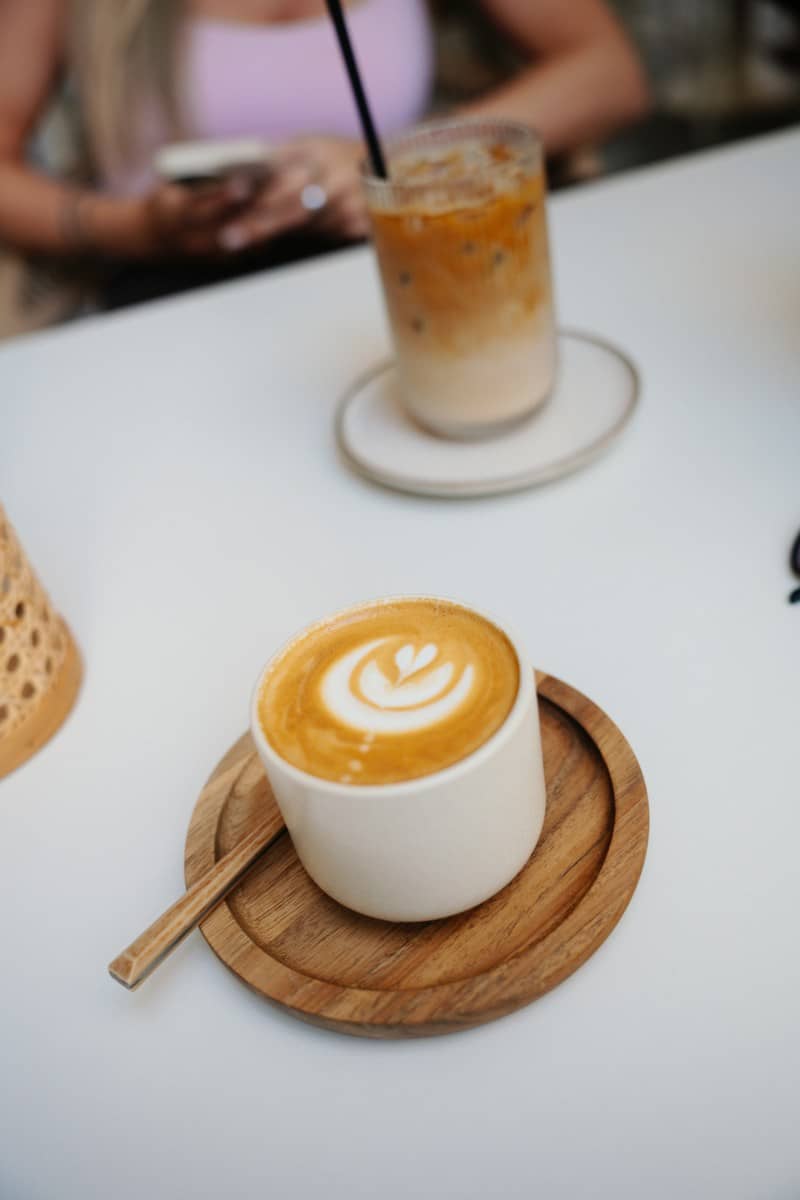 A cup of latte art coffee on a wooden saucer with iced coffee