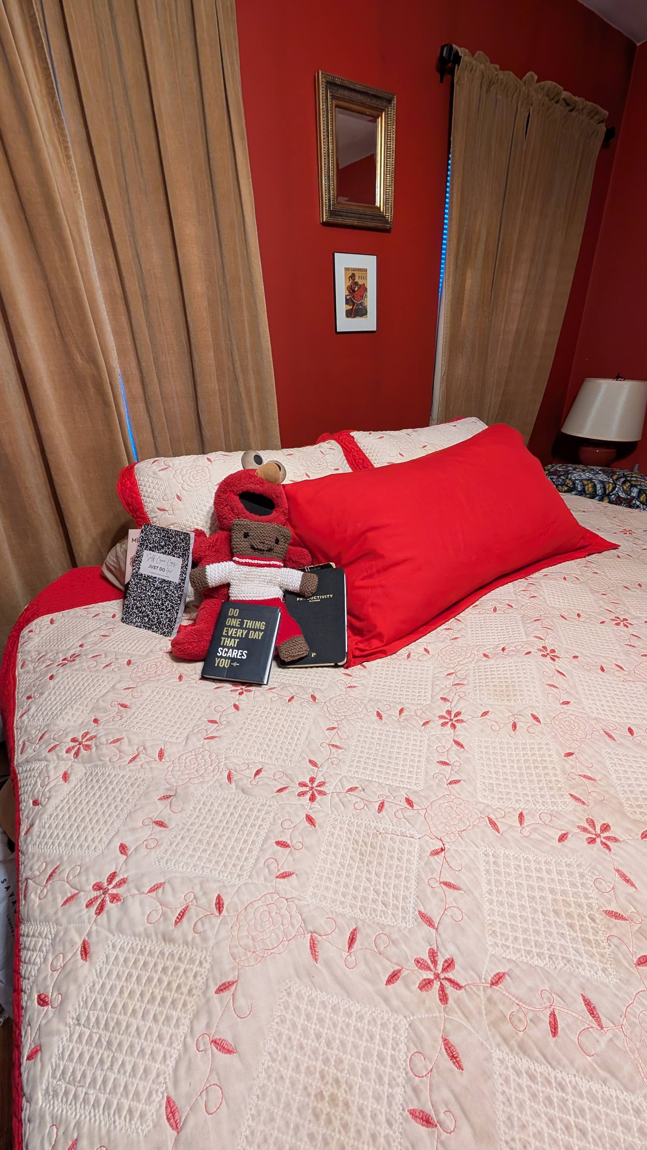 A neatly made bed with red and white bedding, two plush toys, and three journals placed at the center — a warm, personal space that reflects rest, reflection, and nightly ritual.