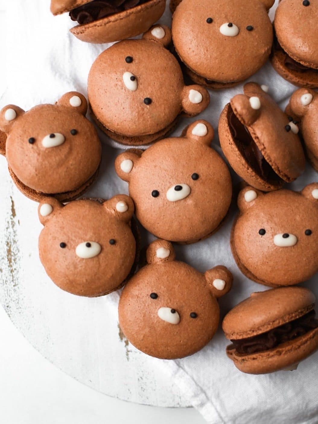 Brown bear macarons filled with a milk chocolate ganache on a white wooden backdrop.