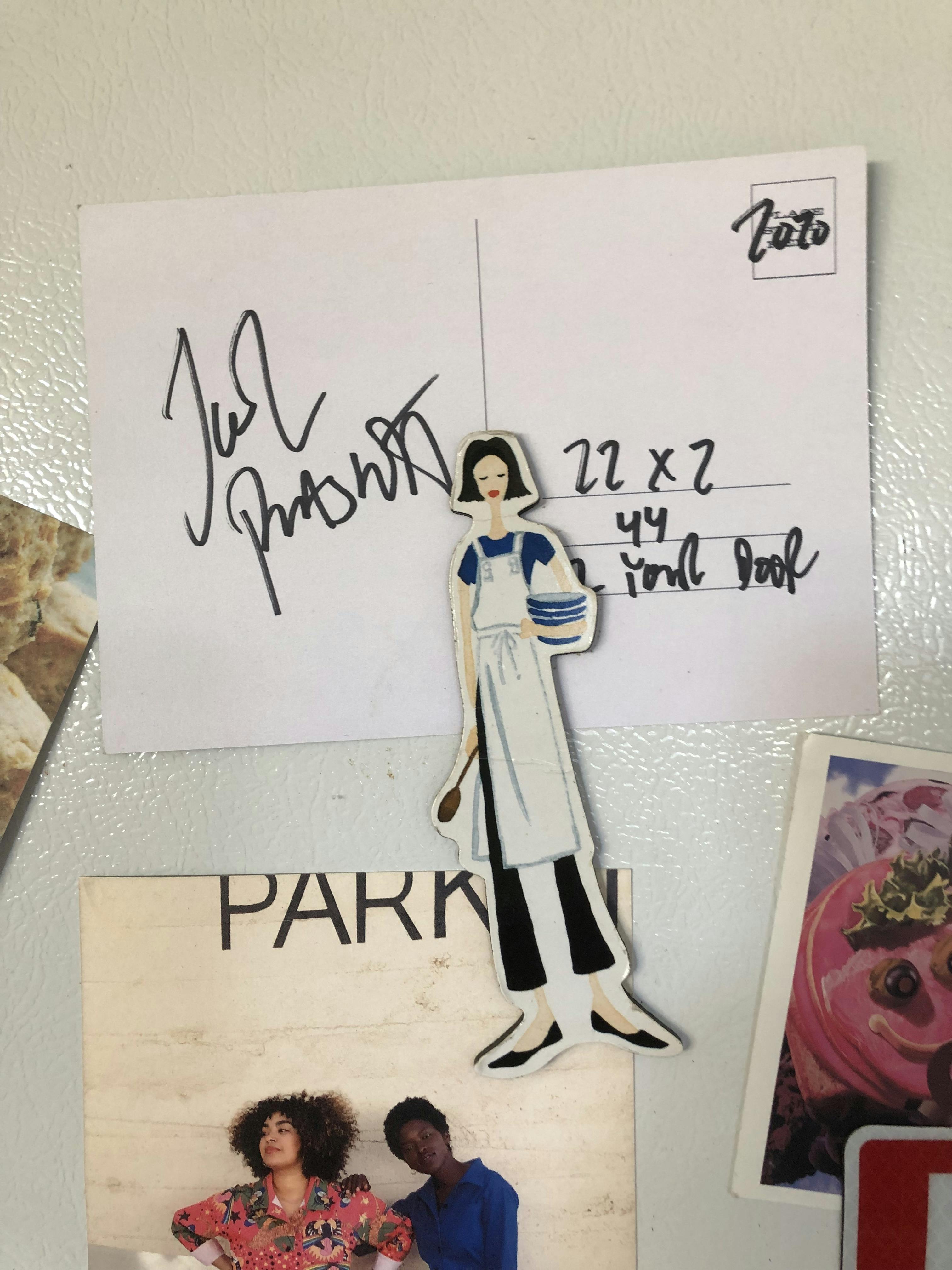 postcard with Joel Plaskett's autograph magneted to a white fridge with a magnet of a baker and other postcards surrounding it