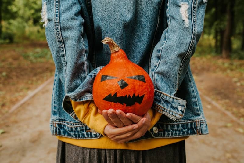Person holding a carved pumpkin with a spooky face.