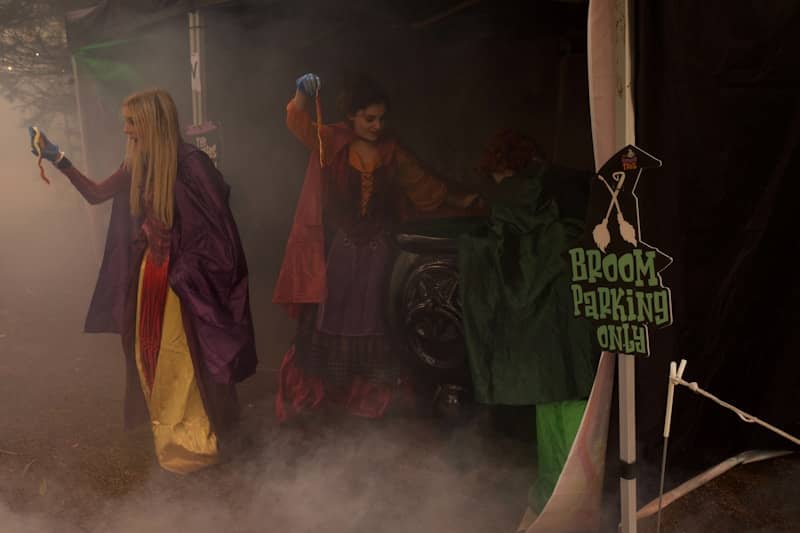 Three women in costumes with a broom parking sign.