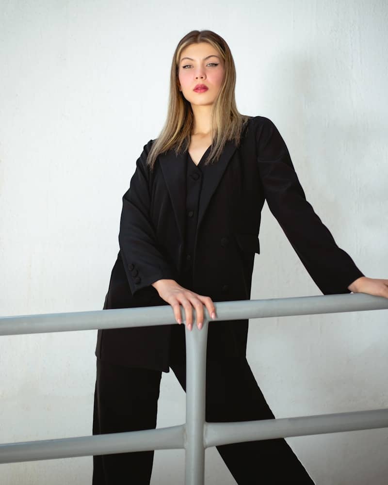 a woman in a black suit leaning on a rail