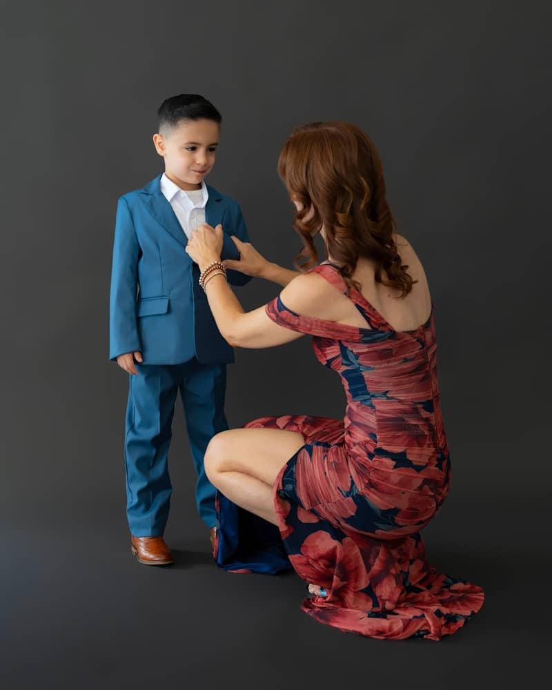 Mother adjusts son's suit jacket on dark background