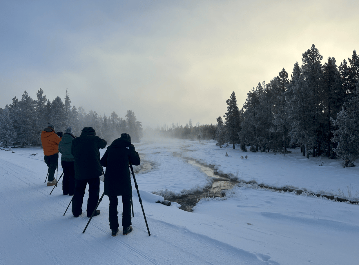 A group of photographers photograph a winter river scene.