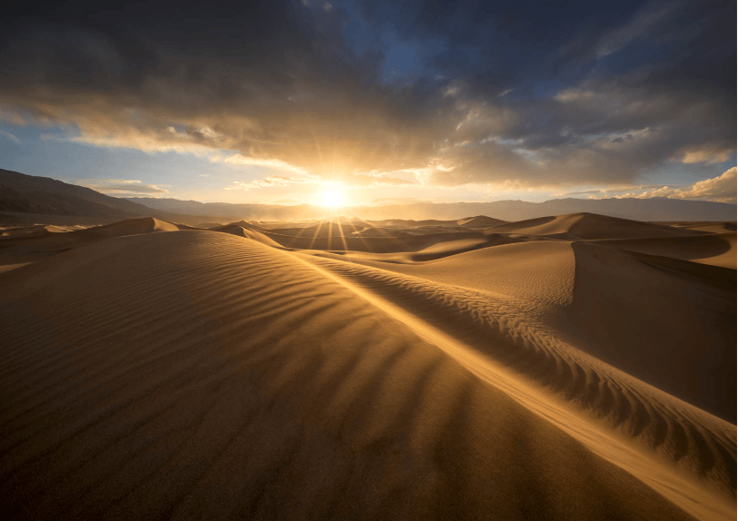 A sand dune set in front of a setting sun in Death Valley National Park. 