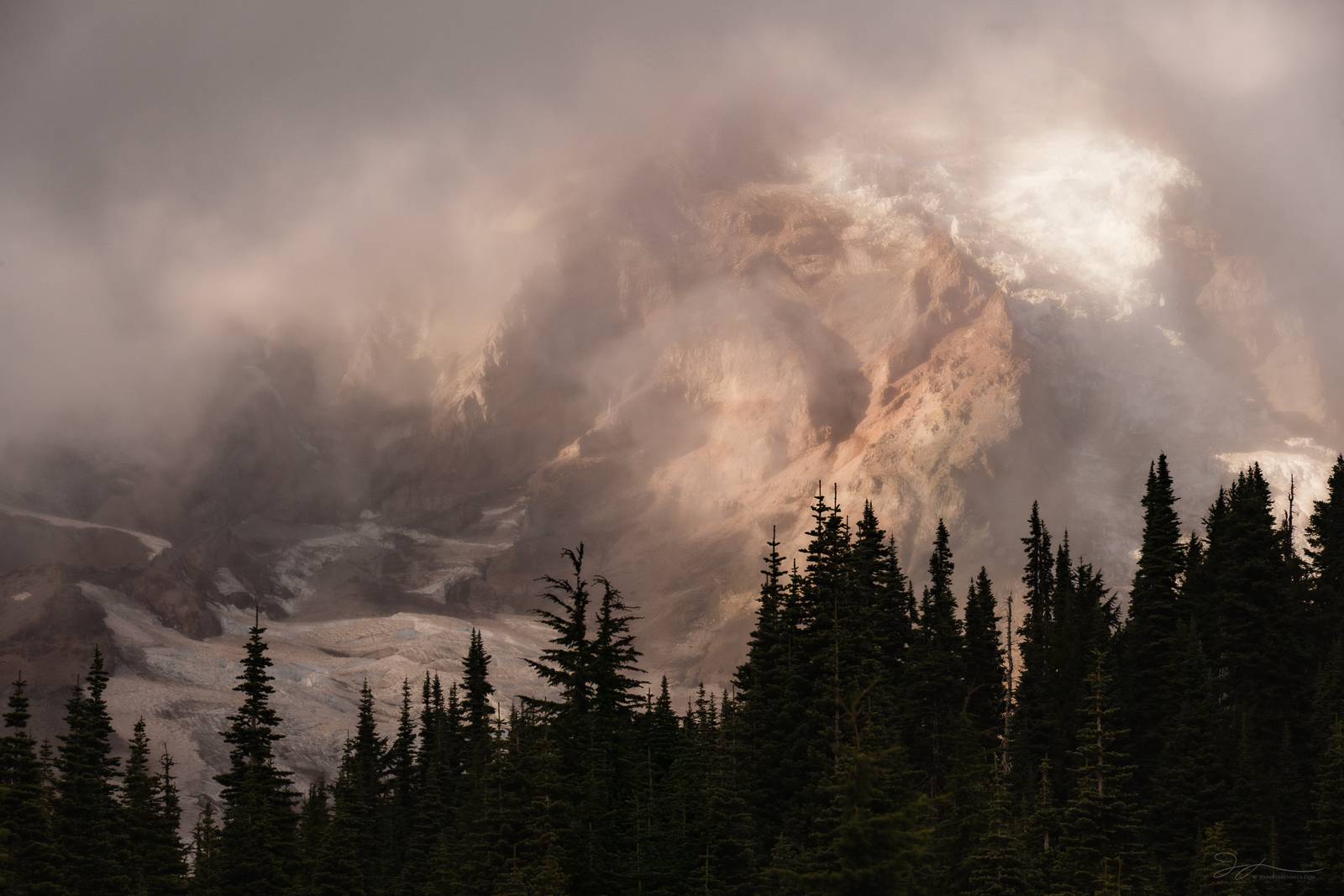 Mt. Rainier sits before a forest of trees as it clears during an autumn storm. 