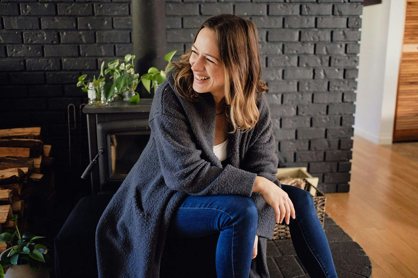 Marie Poulin sitting and laughing in front of a fire place