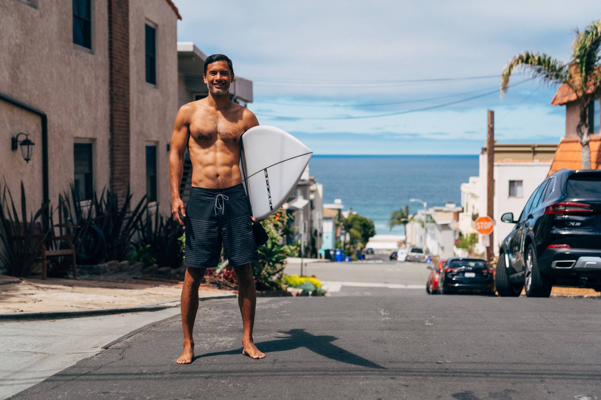 Khe Hy holding a surfboard on a street near the beach