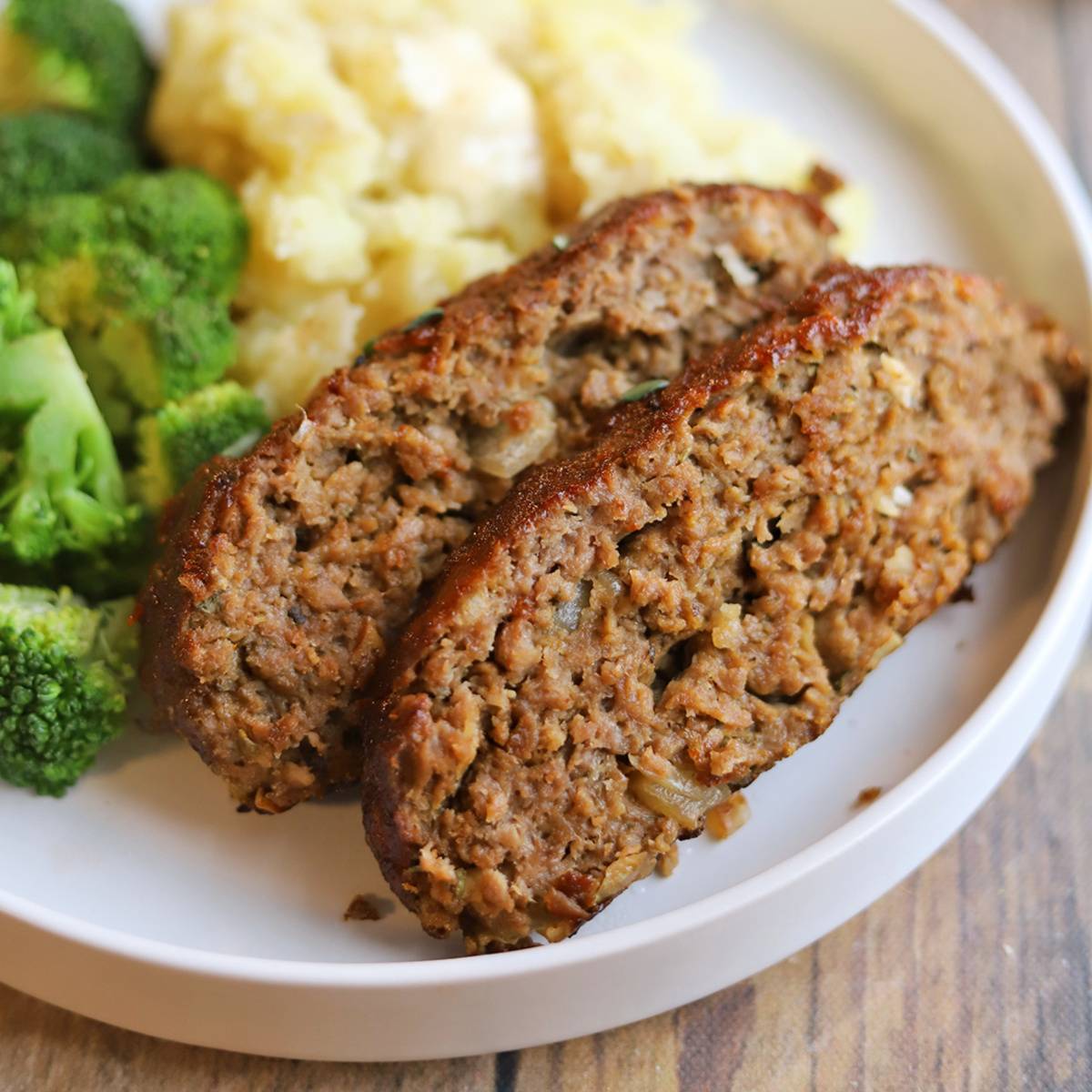 Slices of vegan meatloaf on plate with broccoli and mashed potatoes.