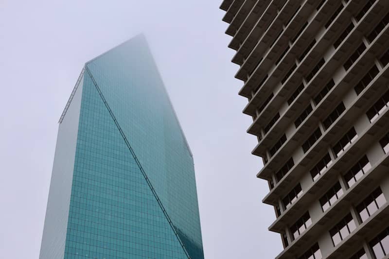 Two modern skyscrapers rise into a foggy sky.