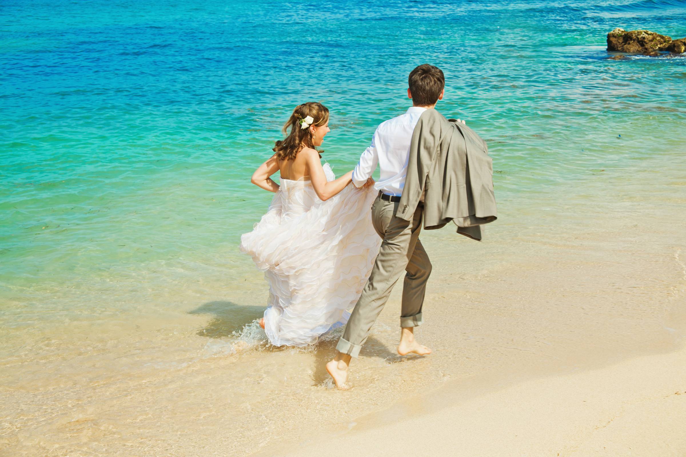 Wedding Couple running along eage of beach