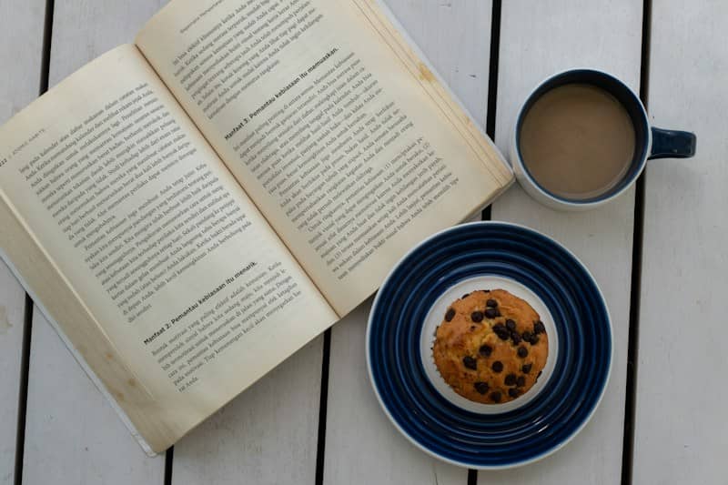 An open book, coffee, and muffin on a white table