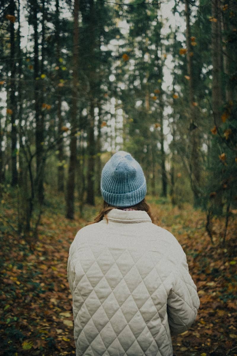 Person wearing a blue beanie walks in a forest.