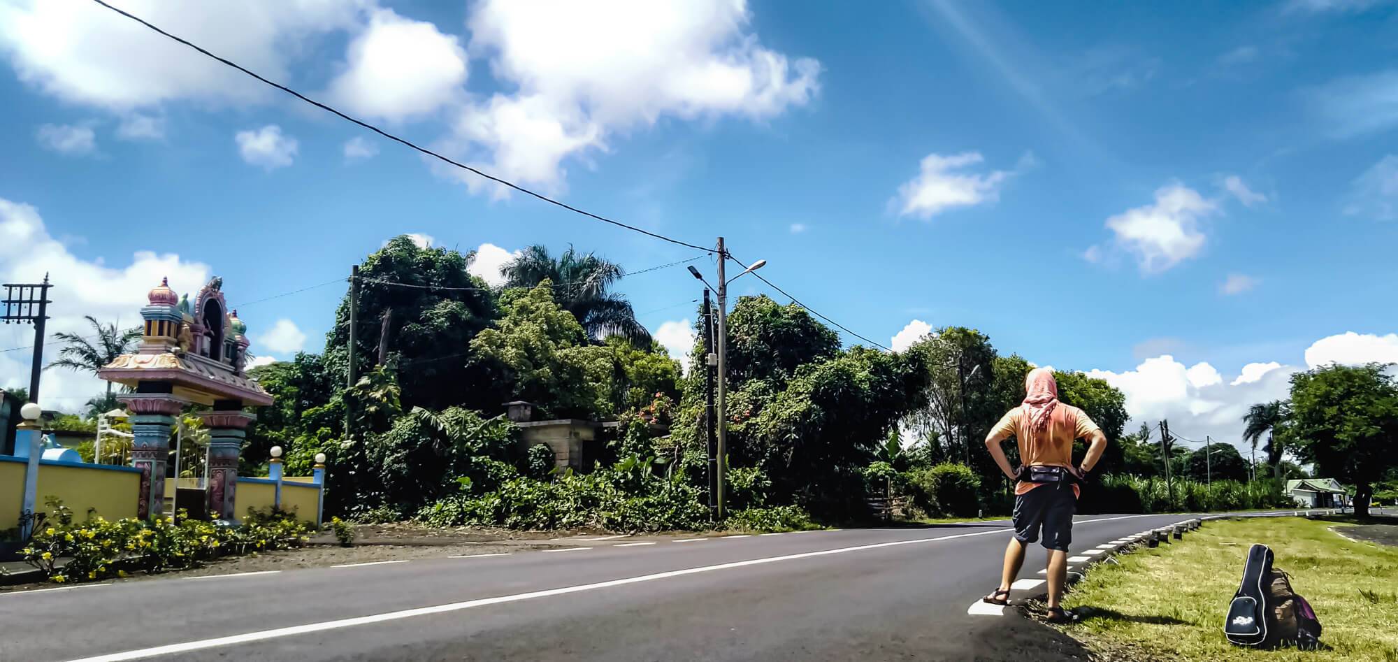 A backpacker hitchhiking in front of a temple on a tropical isaland