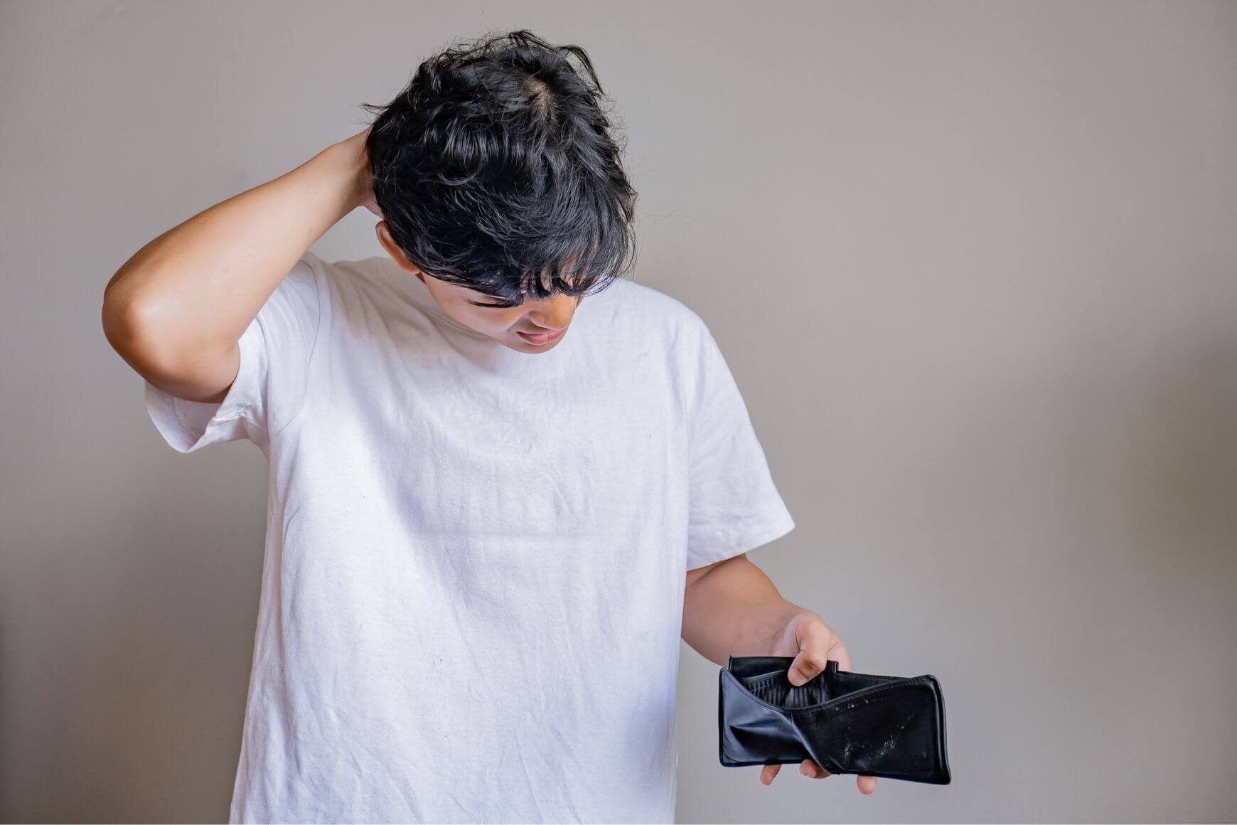 broke young man looking at his empty wallet
