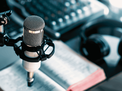 An image of a condenser mic on a shock mount, with blurred headphones and a book just behind the main image.