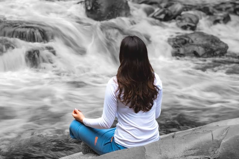 A woman sitting on a rock in front of a river