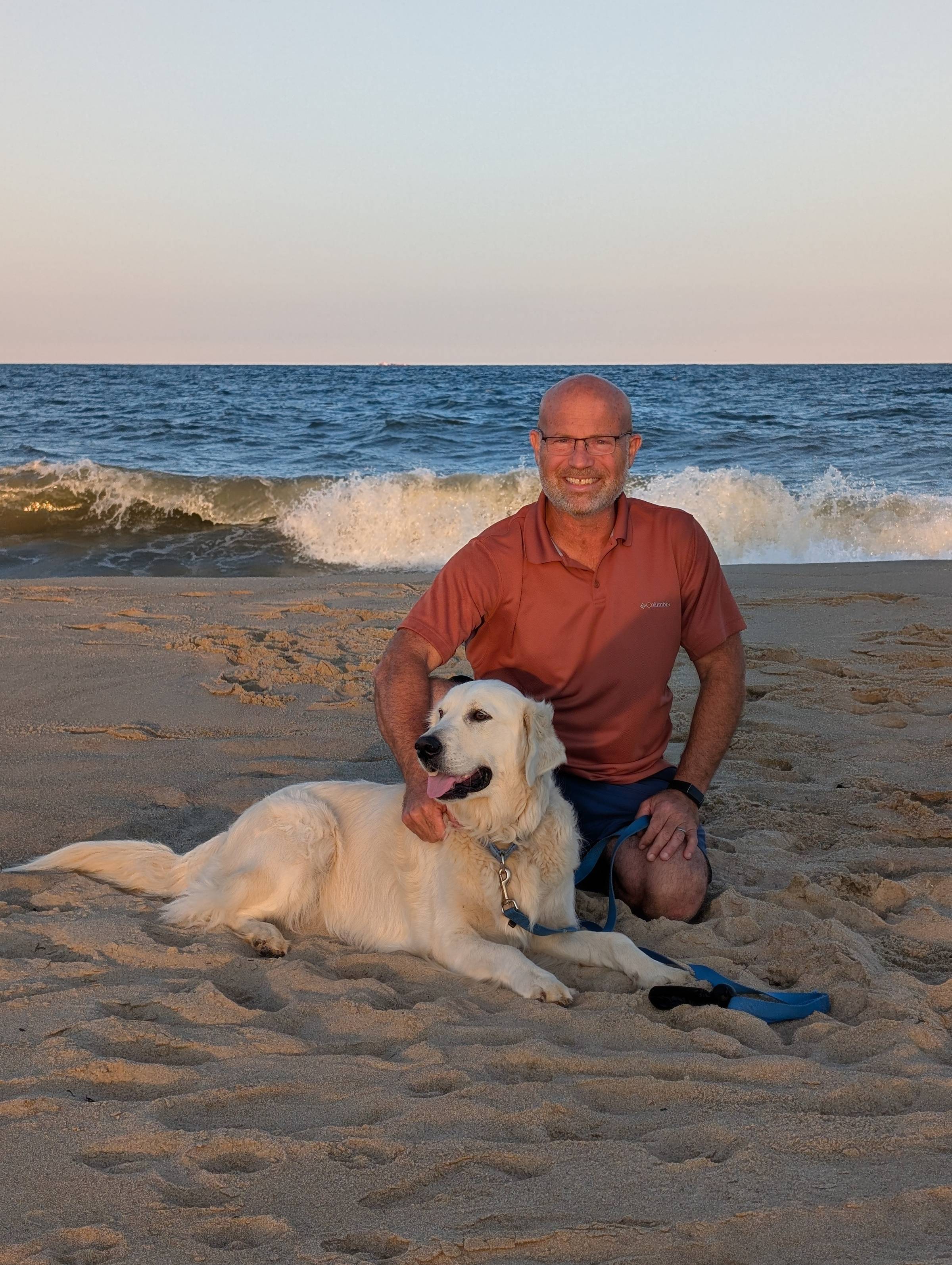 Picture of Billy at the ocean with waves behind him and his Golden Retriever named Yeti