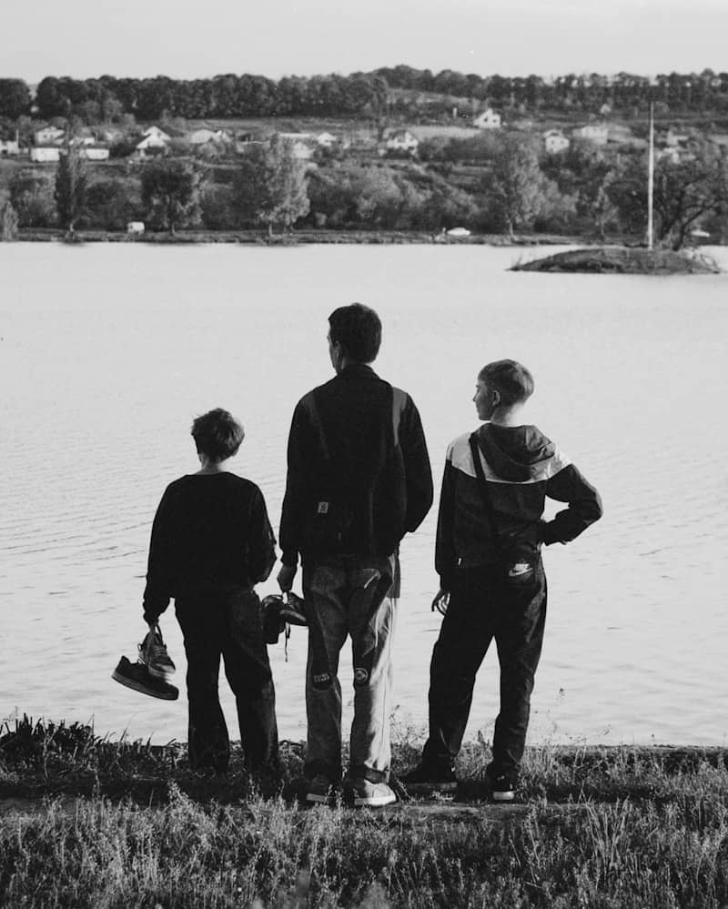 Three boys stand by a lake looking at the landscape.
