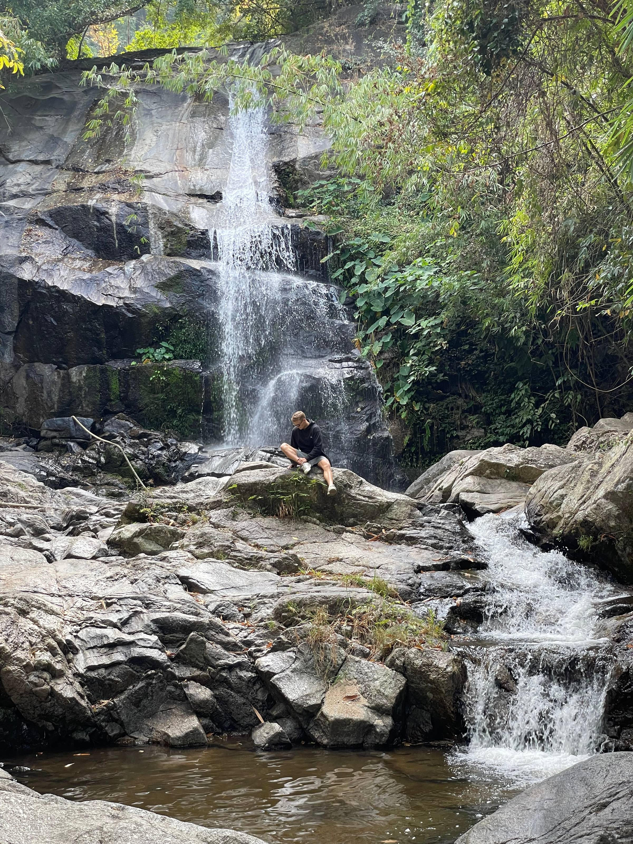 man sitting on a rock next to waterfall
