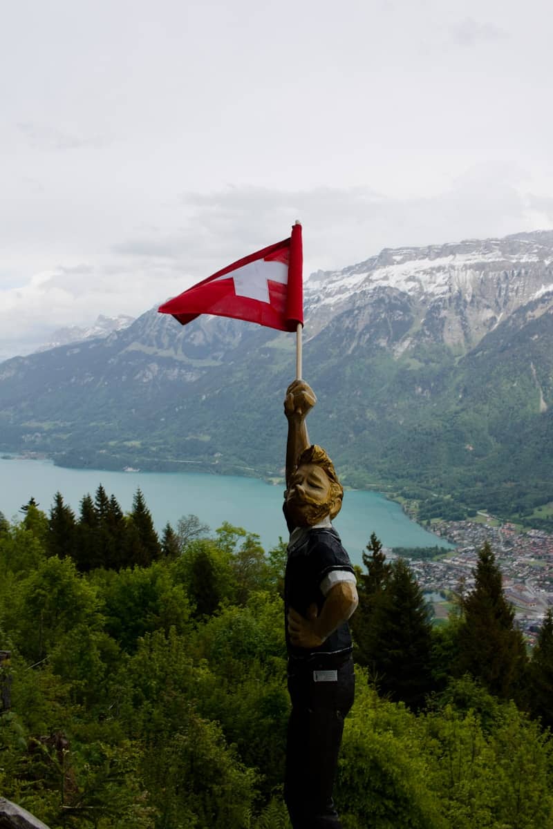 Wooden statue holding swiss flag overlooking lake and mountains.