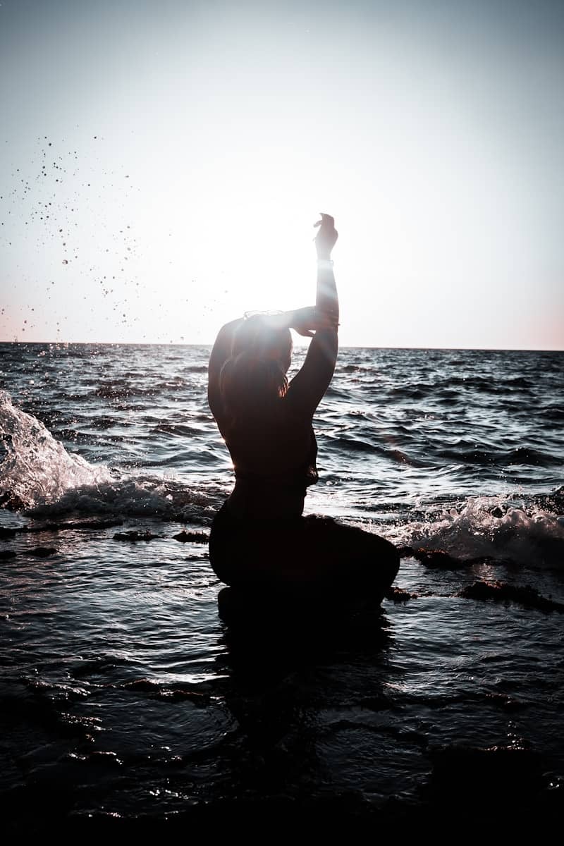 A person kneels by the water, silhouetted.