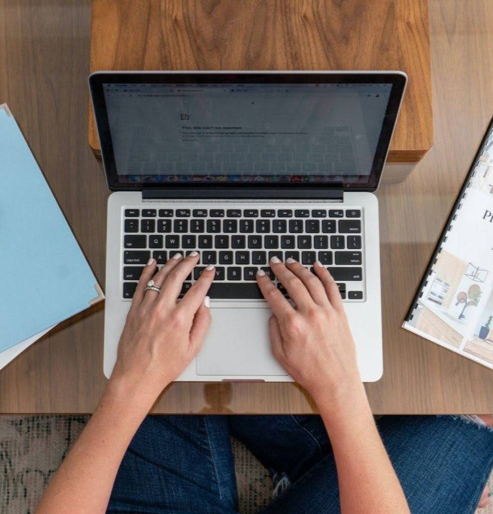 hands typing on a laptop with a notebook on the desk