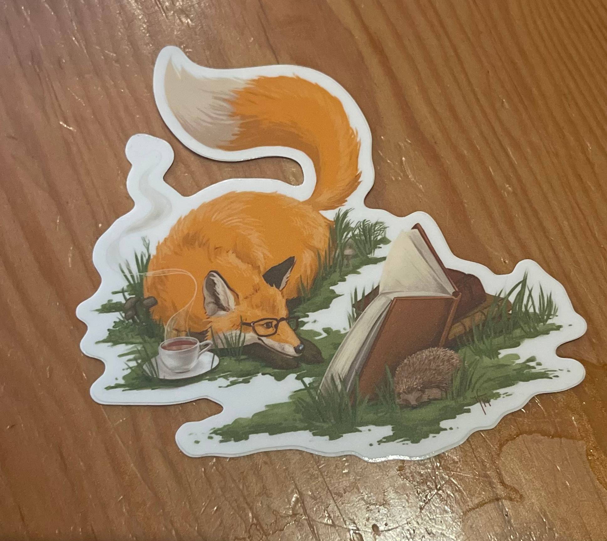 Image of a sticker with an illustration of a red fox wearing glasses and reading a book.