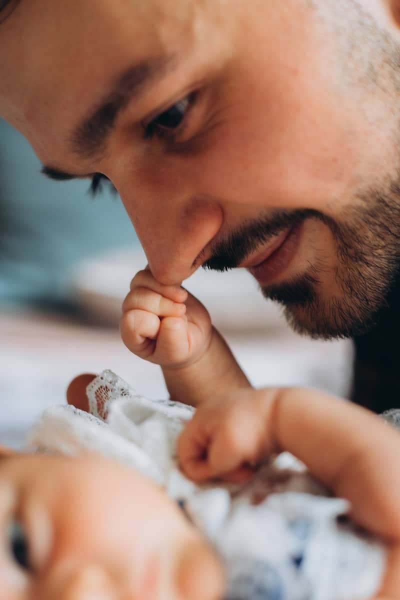Baby's hand gently touches a bearded man's nose.