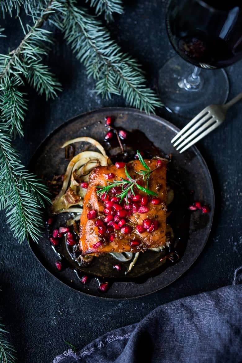 Salmon with pomegranate seeds and fennel on a black plate with a fork.