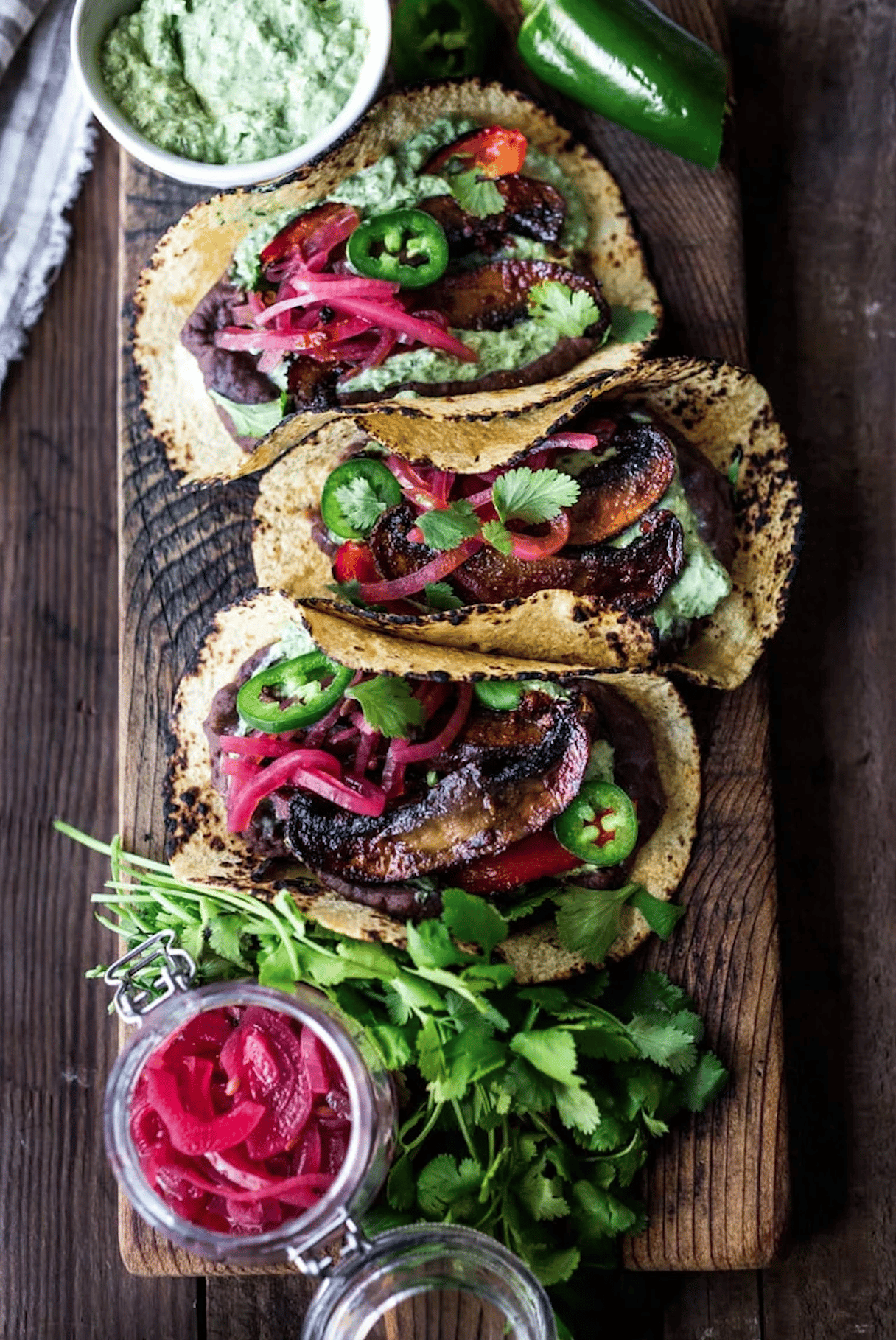 portobello tacos with pickled onions on a long wood board.