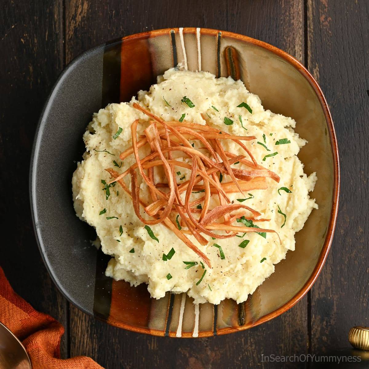 A ceramic plate with mashed parsnips topped with crispy fried parsnips and parsley.