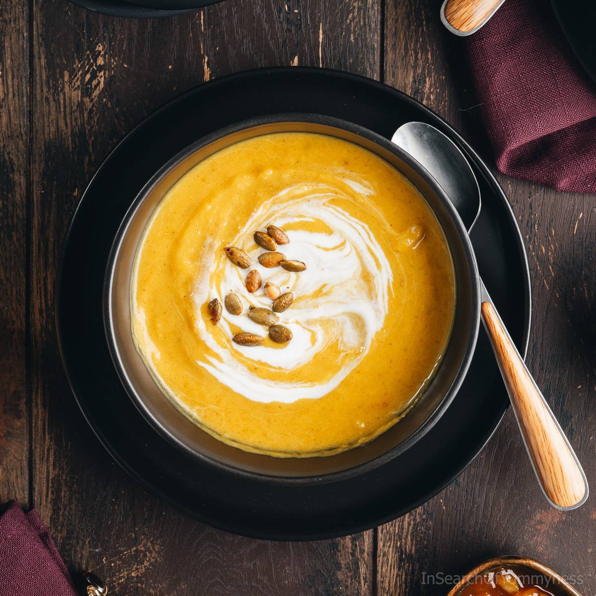 Overhead view of a bowl of butternut squash soup garnished with pumpkin seeds and a swirl of coconut milk.